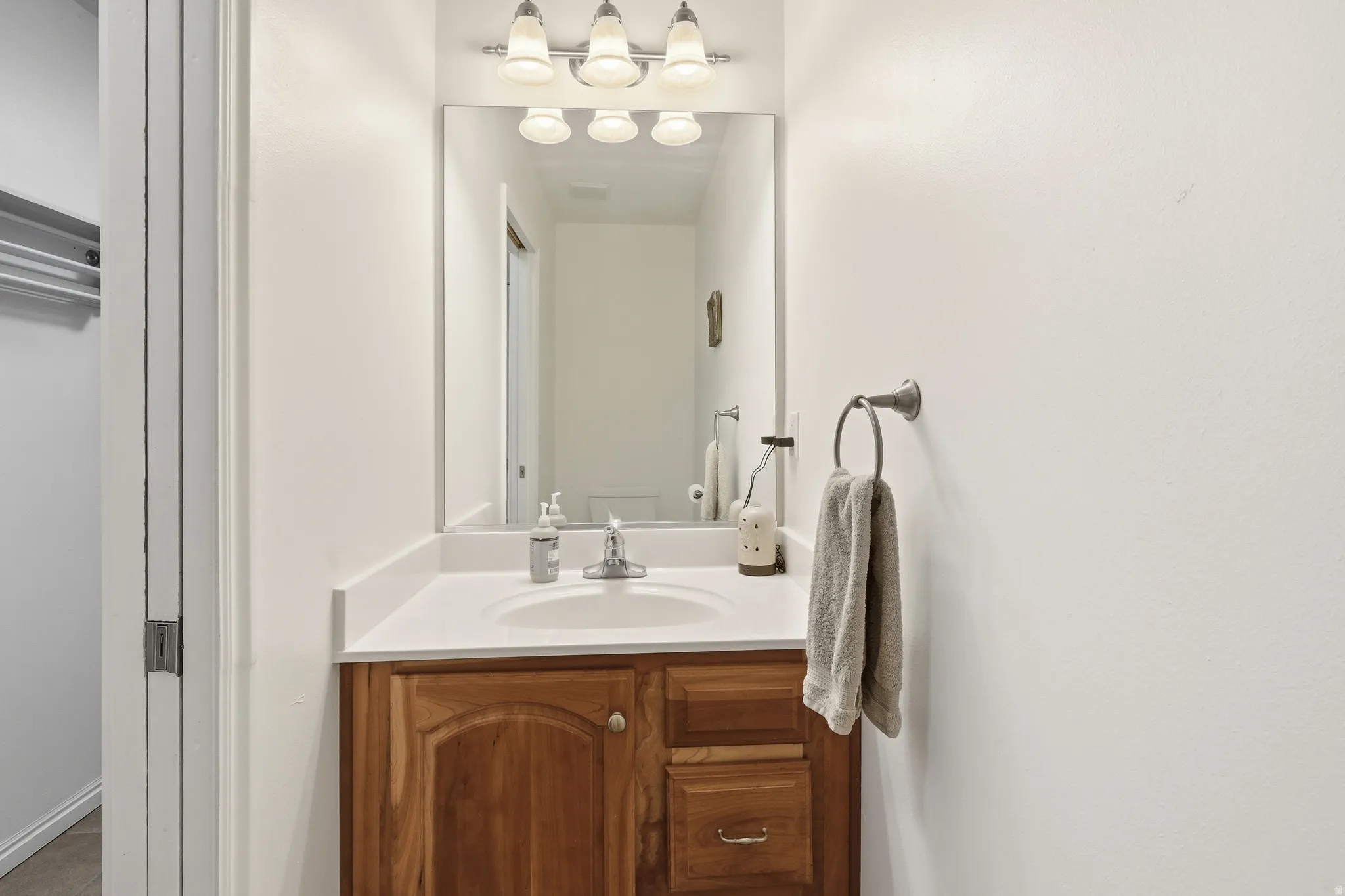 Bathroom vanity featuring a wood-finish cabinet, white countertop, and a single basin sink with a chrome faucet