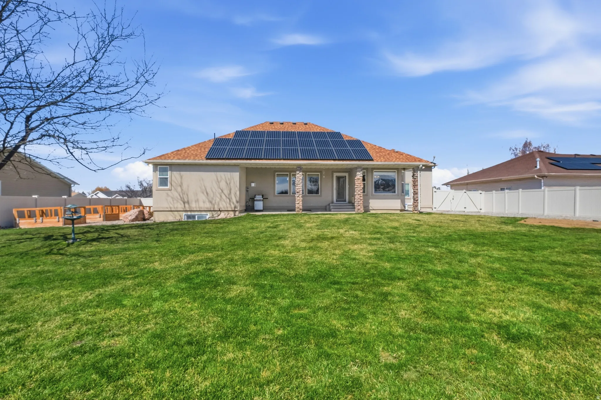 Expansive green lawn with a stucco and brick exterior residence featuring solar panels, covered patio, and a wood deck