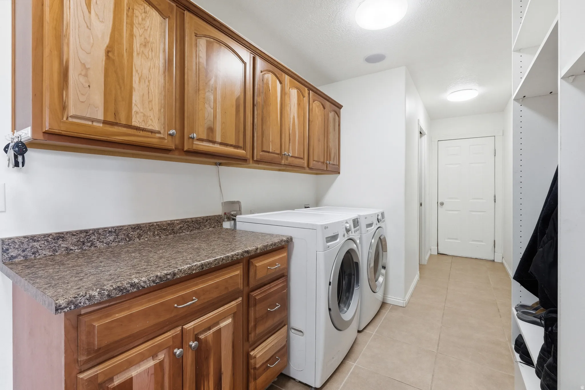 Laundry area featuring wood-finish cabinetry, a speckled countertop, and tiled flooring