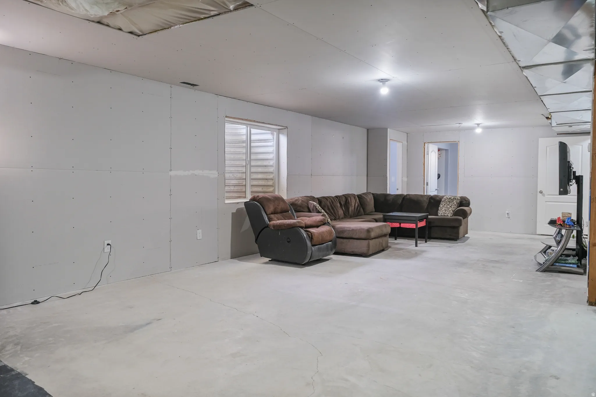 Lower level space featuring unfinished drywall, exposed ceiling joists with insulation, a single window, and concrete flooring