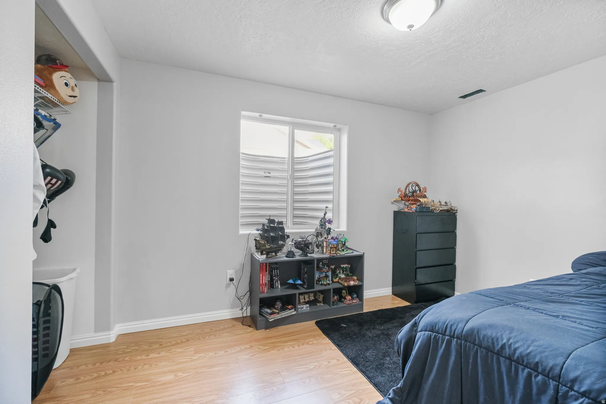 Room featuring a window with a window well, wood-finish flooring, and white baseboards