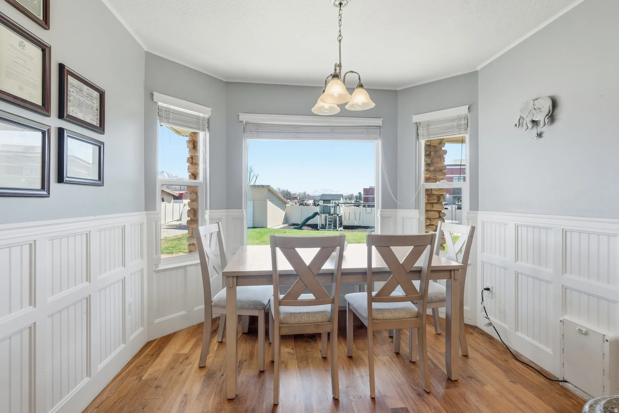 Bay window dining area featuring wood-finish flooring and white wainscoting