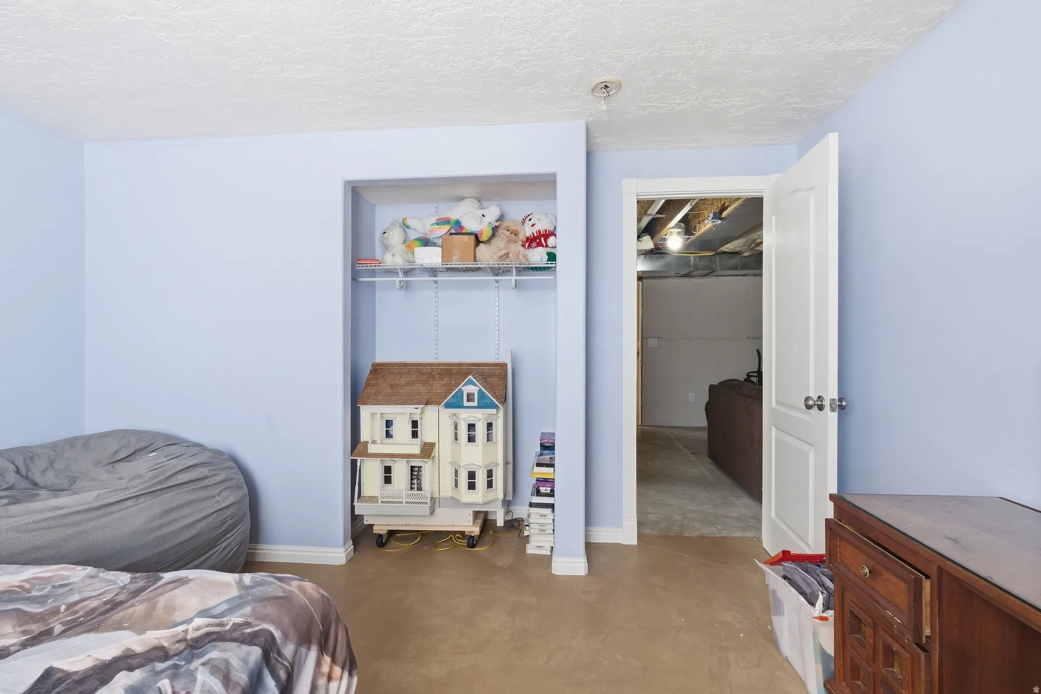 Room featuring light blue walls, textured ceiling, and an open doorway leading to an unfinished space
