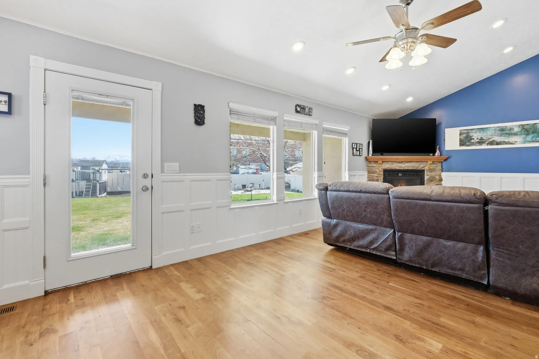 Living area featuring wood-finish flooring, white wainscoting, and a fireplace with a stone surround