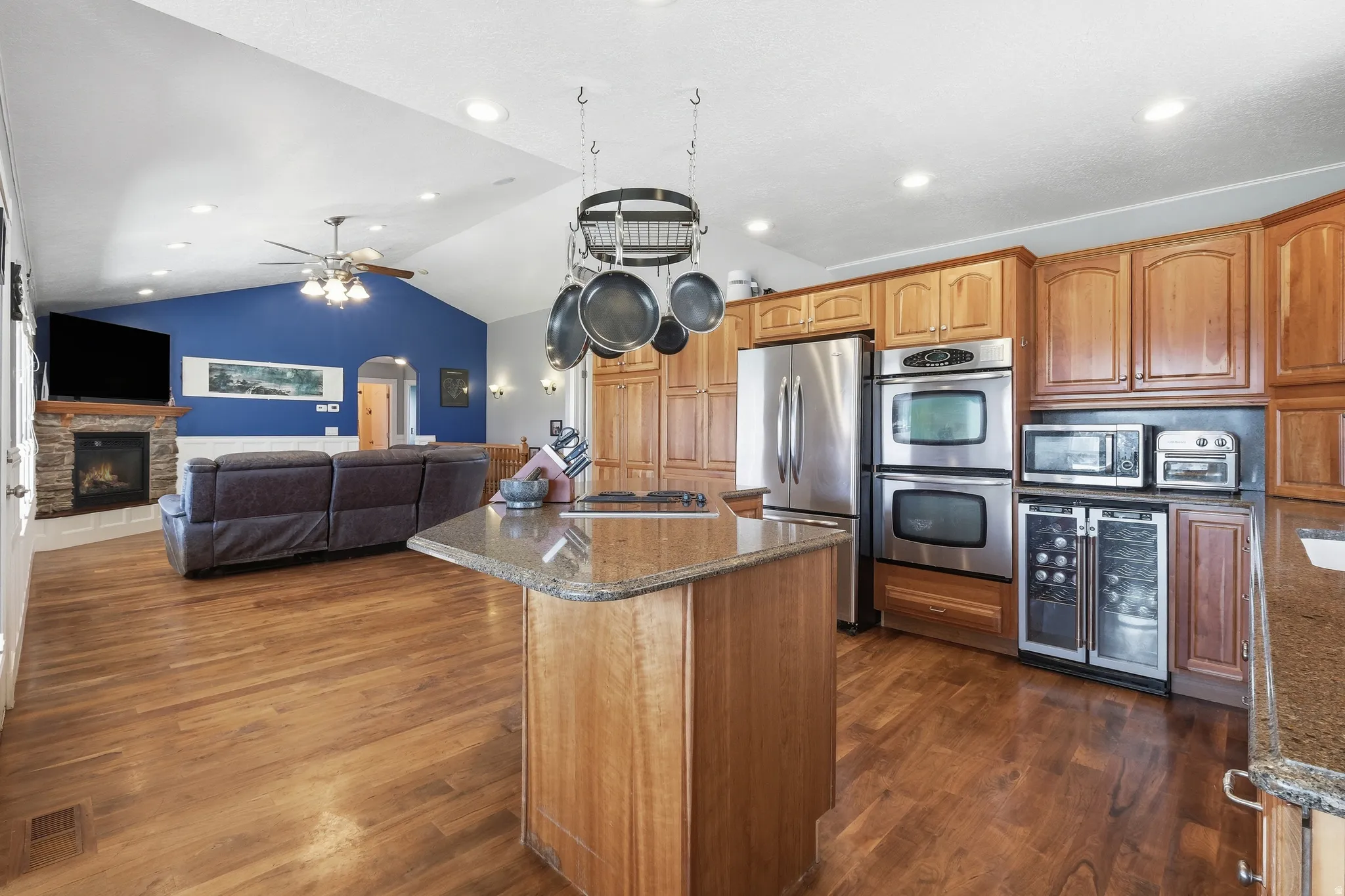 Open-concept living space featuring wood-finish flooring, a stone-surround fireplace, and vaulted ceilings with recessed lighting