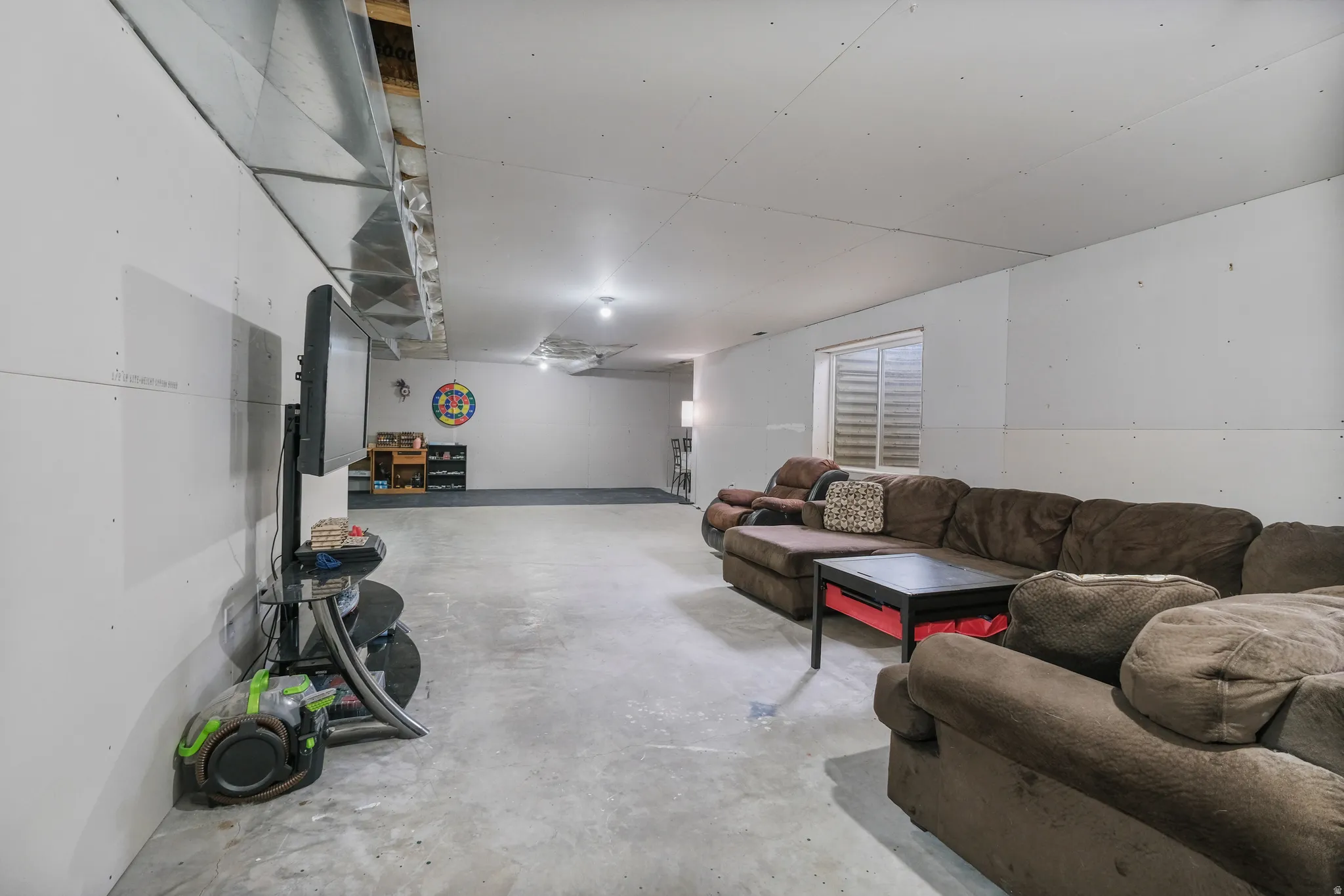 Expansive finished basement featuring concrete flooring and white walls, with recessed lighting and a window with horizontal blinds