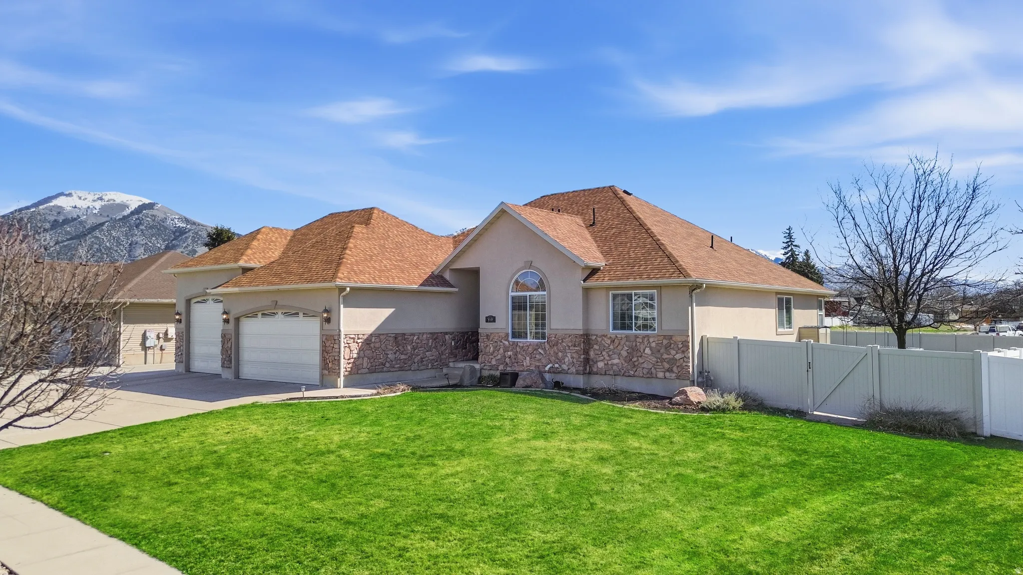 Exterior featuring stucco siding with stone accents, a multi-car garage, a well-maintained lawn, and a light-colored privacy fence