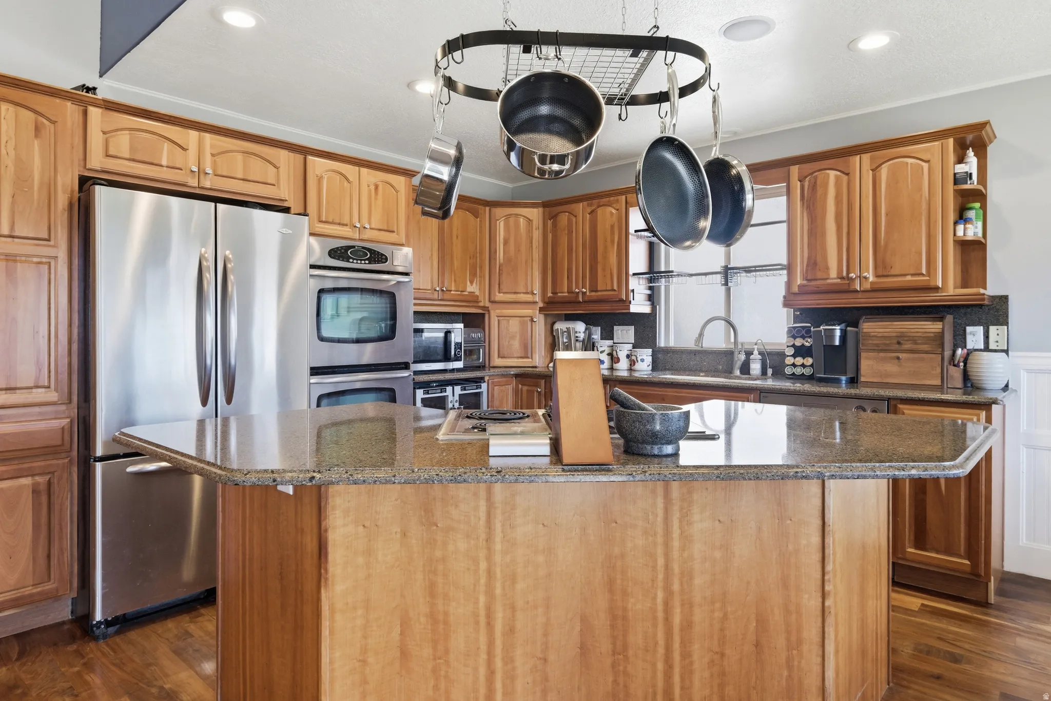 Kitchen featuring a central island with a stone-finish countertop, wood cabinetry, stainless steel appliances including a double oven and refrigerator, and recessed lighting