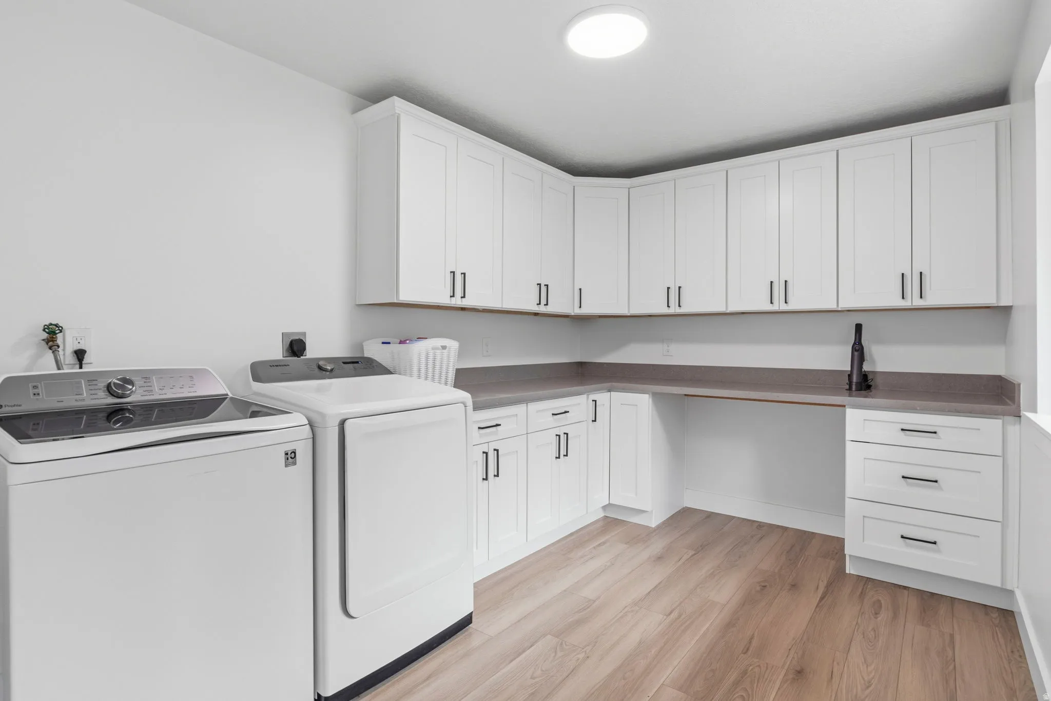 Dedicated laundry space featuring extensive white cabinetry, durable countertops, wood-finish flooring, and a circular ceiling light fixture