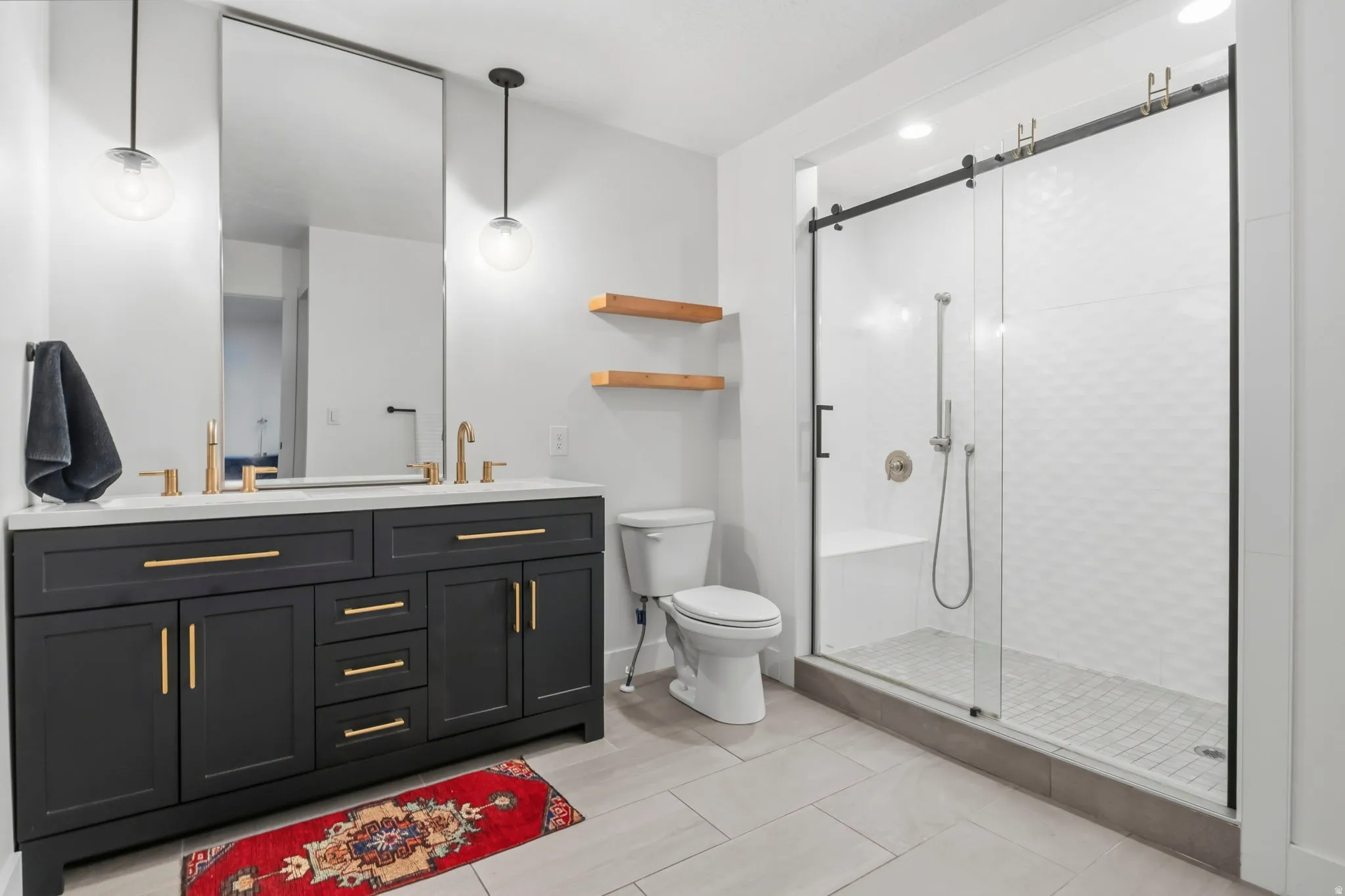 Modern bathroom featuring a double vanity with dark cabinetry, gold-finish hardware, and a light-toned countertop