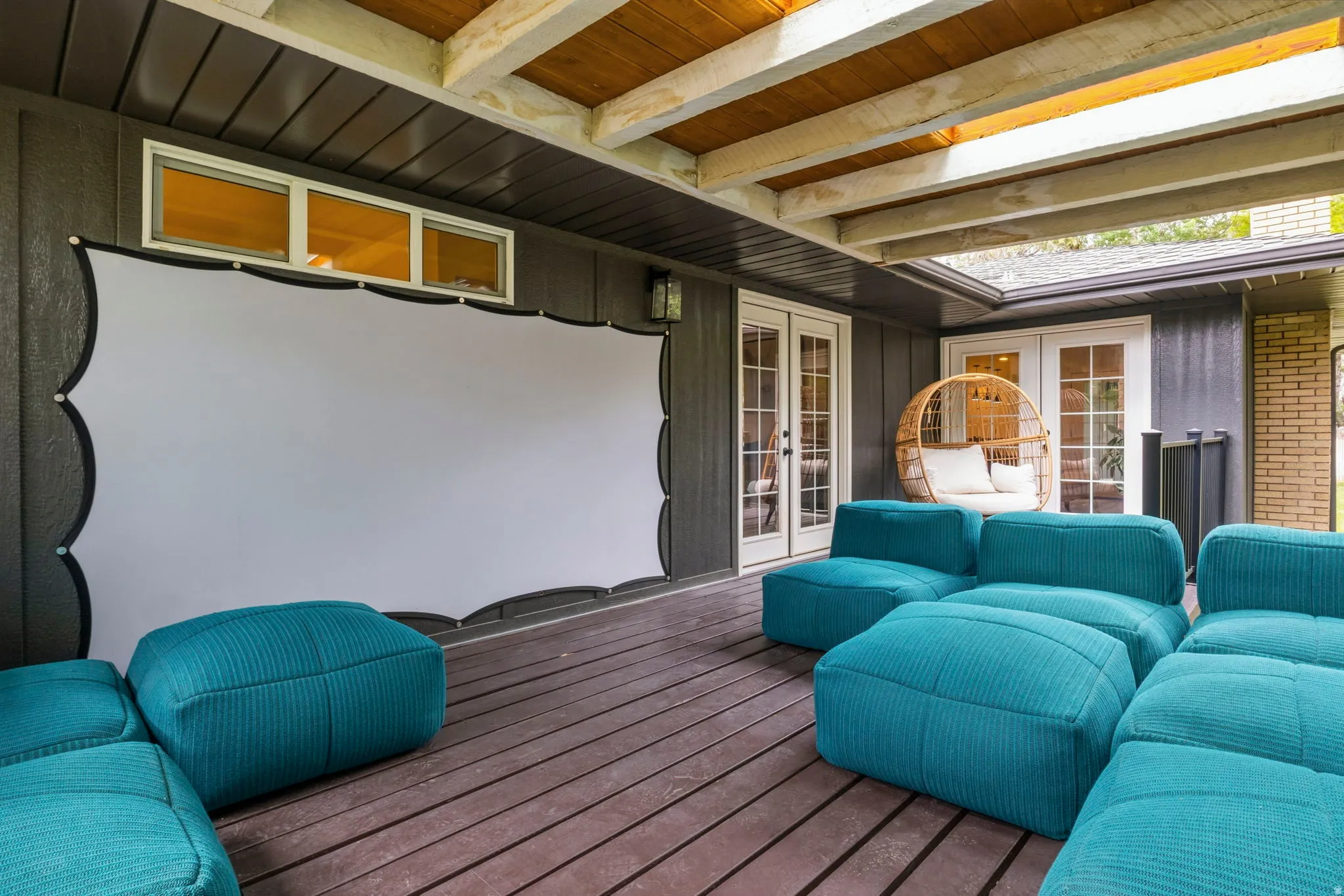 Covered outdoor patio featuring a large projection screen, two sets of French doors, wood-finish decking, and an exposed beam ceiling