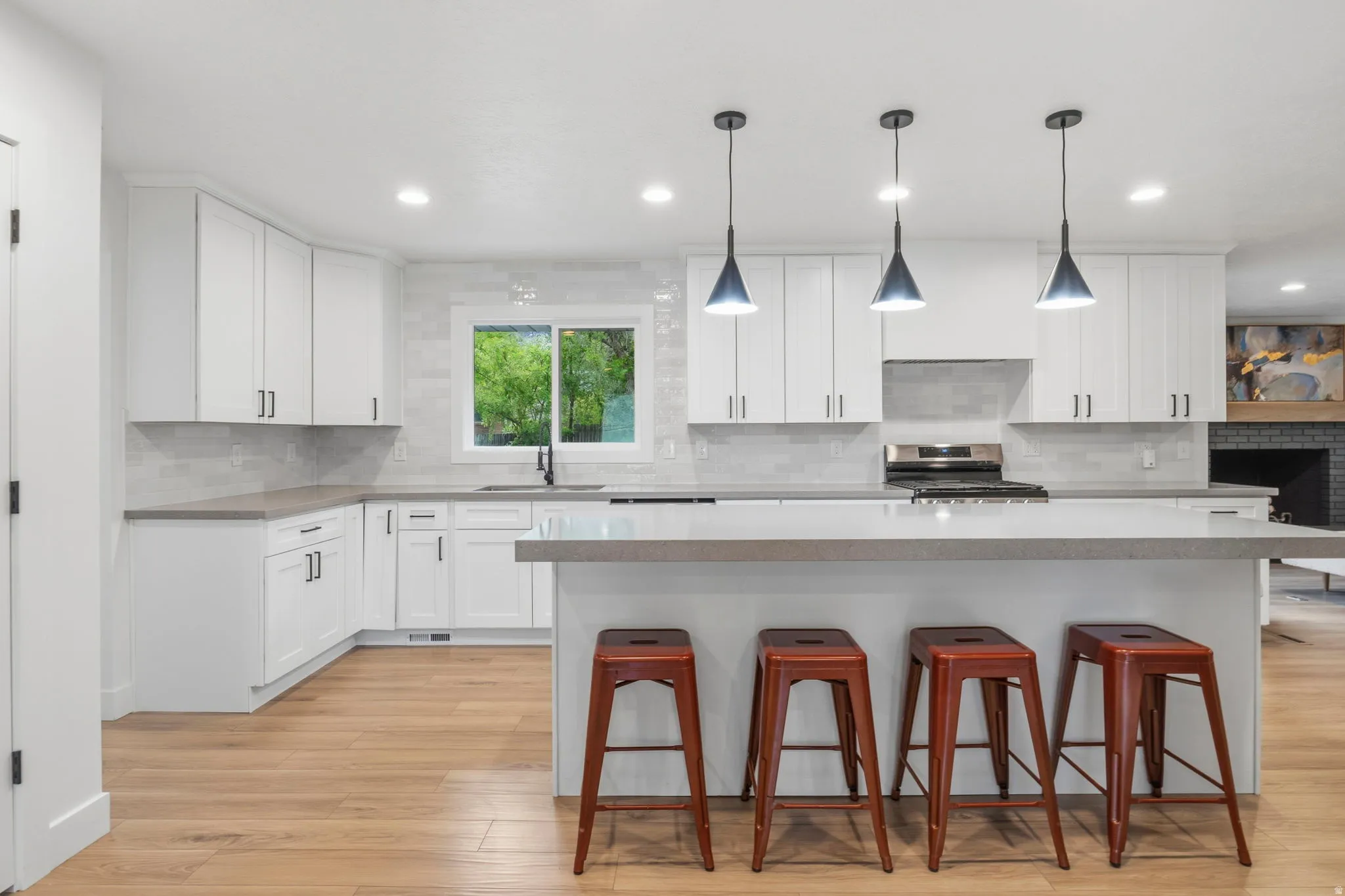 Modern kitchen featuring an expansive island with a light-toned countertop, white shaker-style cabinetry, and wood-finish flooring