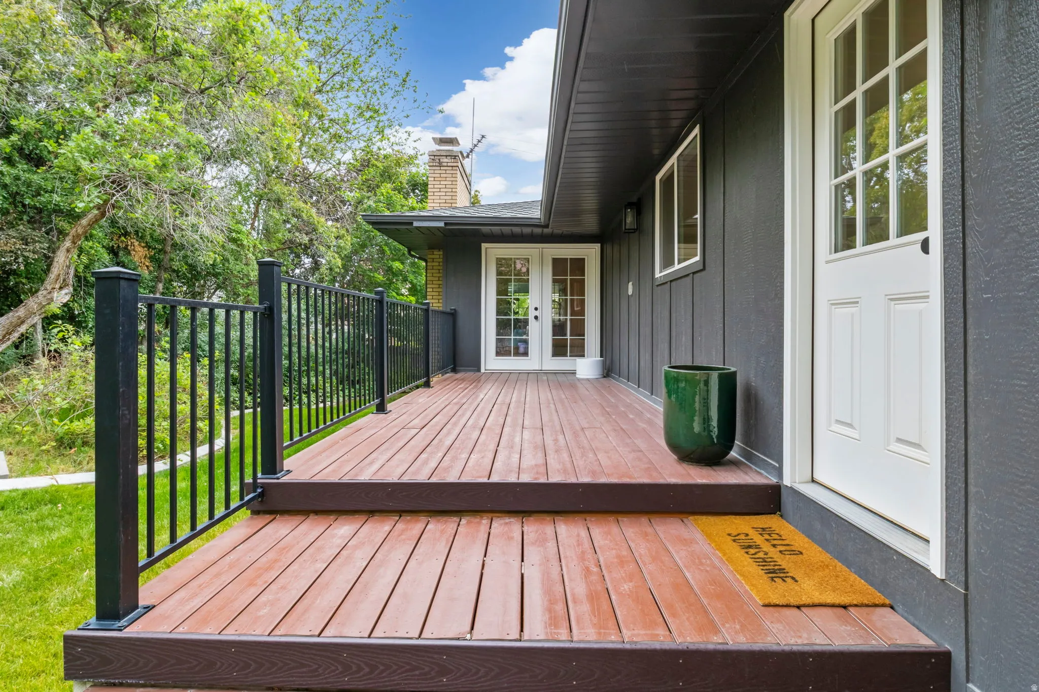 Expansive wood-finish deck with black metal railing, featuring a white paneled door with glass inserts and an additional set of white French doors
