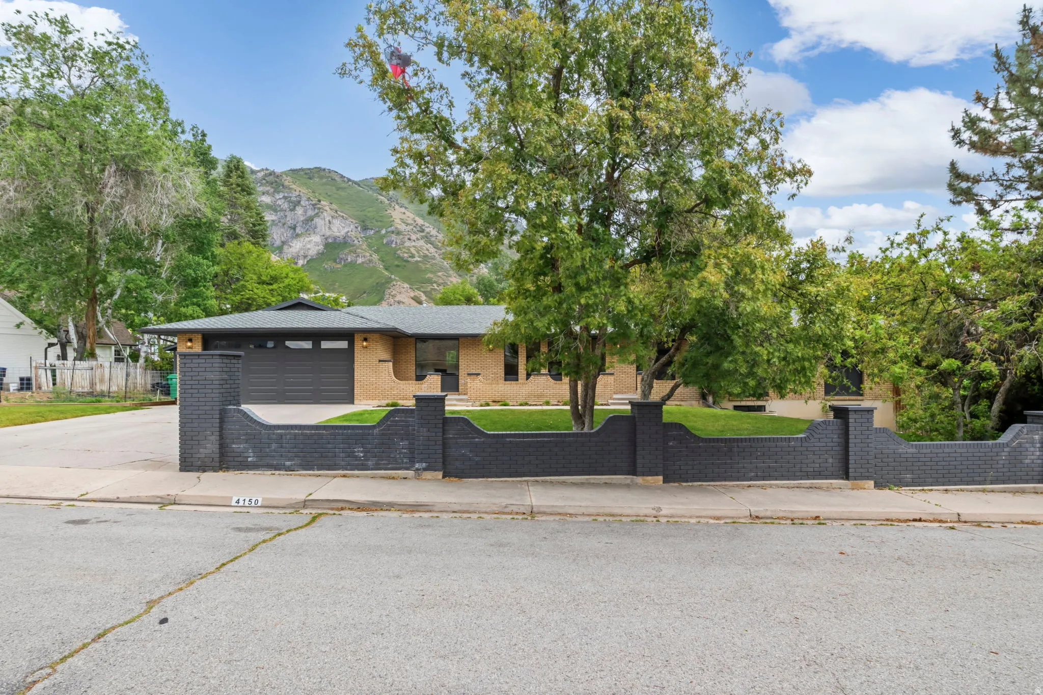 Ranch-style residence featuring a distinctive dark brick privacy wall and an attached garage with a dark panel door