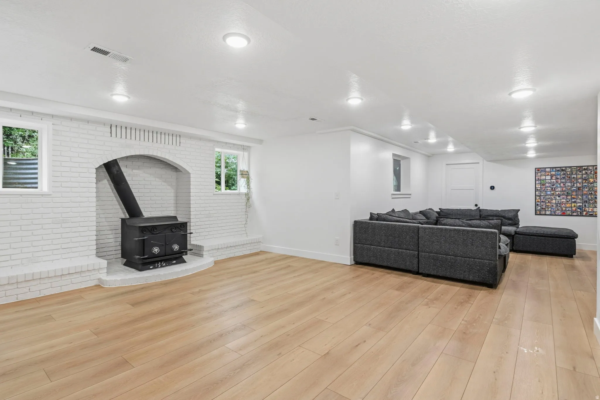 Spacious room featuring a white painted brick fireplace with a black wood stove insert, light wood-finish flooring, and recessed ceiling lighting