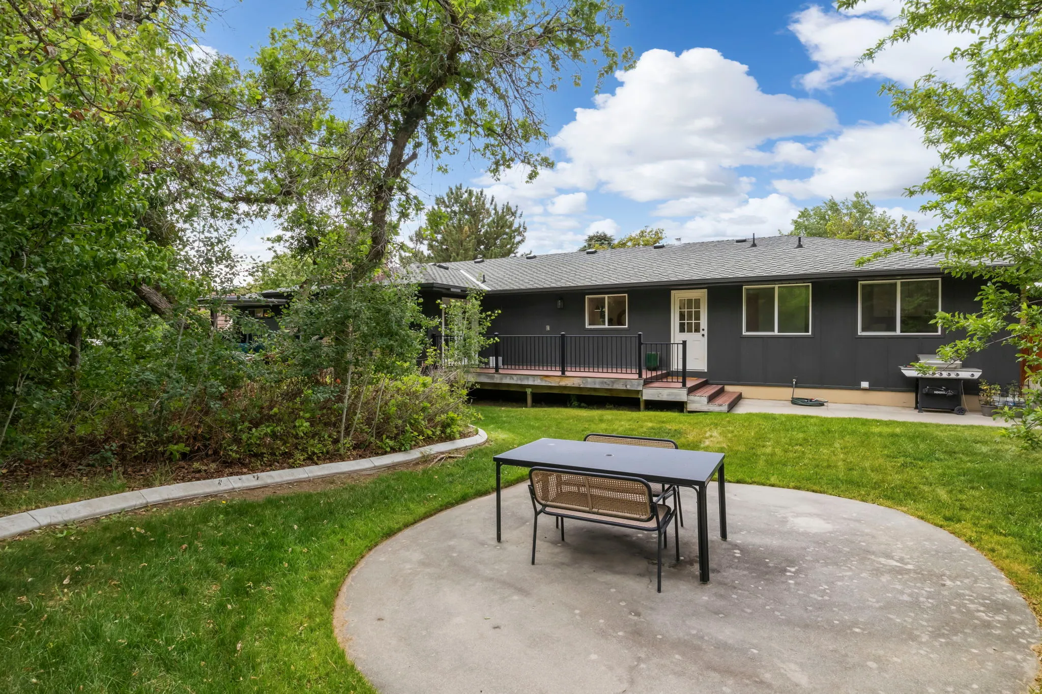 Spacious backyard featuring a large concrete patio, expansive lawn, and mature trees