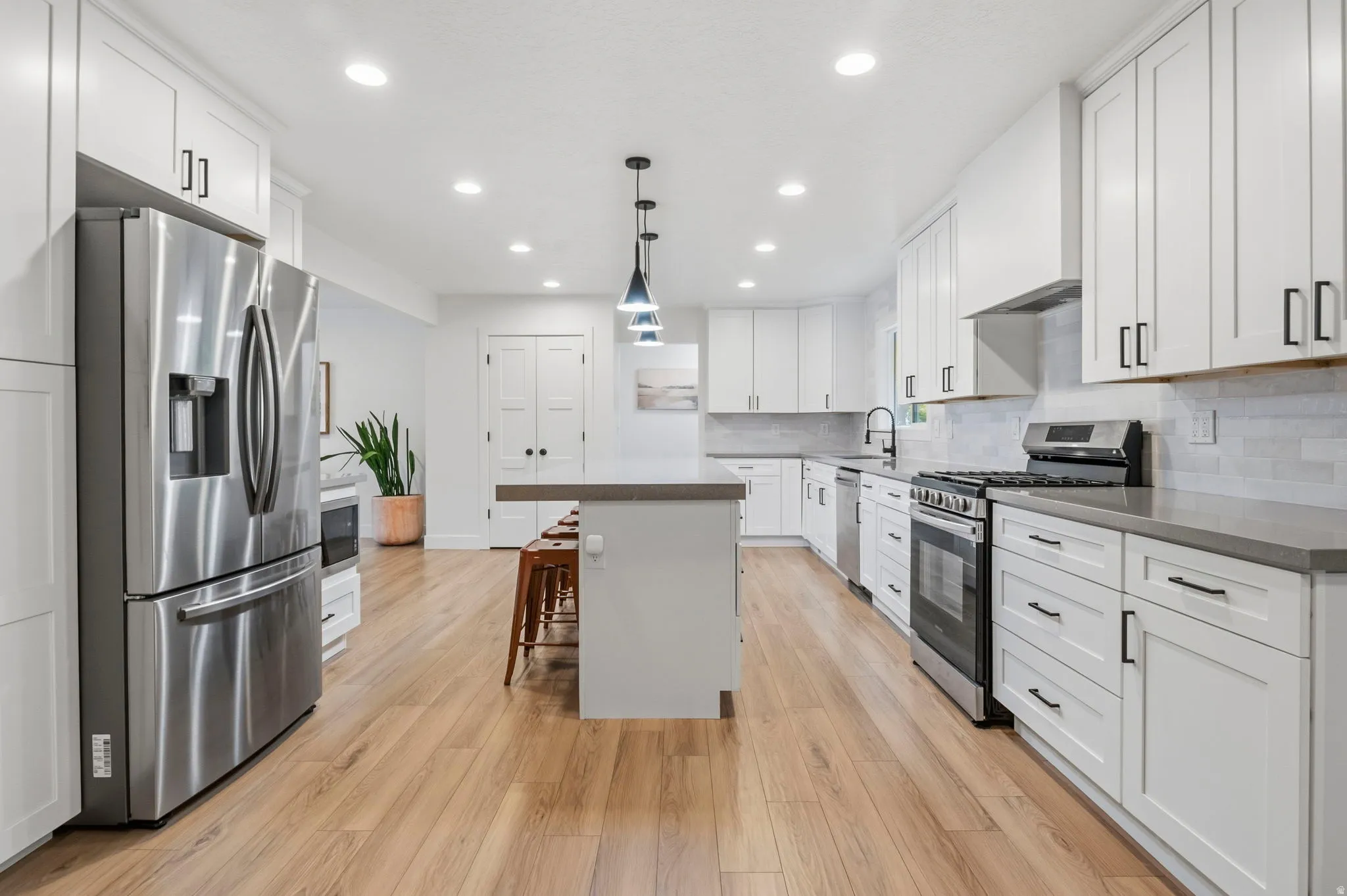 Spacious kitchen featuring extensive white cabinetry, stainless steel appliances, wood-finish flooring, a central island, and recessed lighting