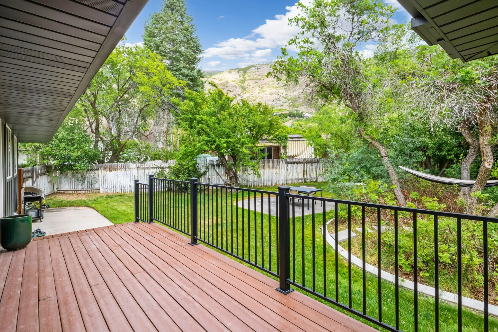 Expansive wood-finish deck with black metal railings, overlooking a verdant backyard with mature trees and a fenced perimeter