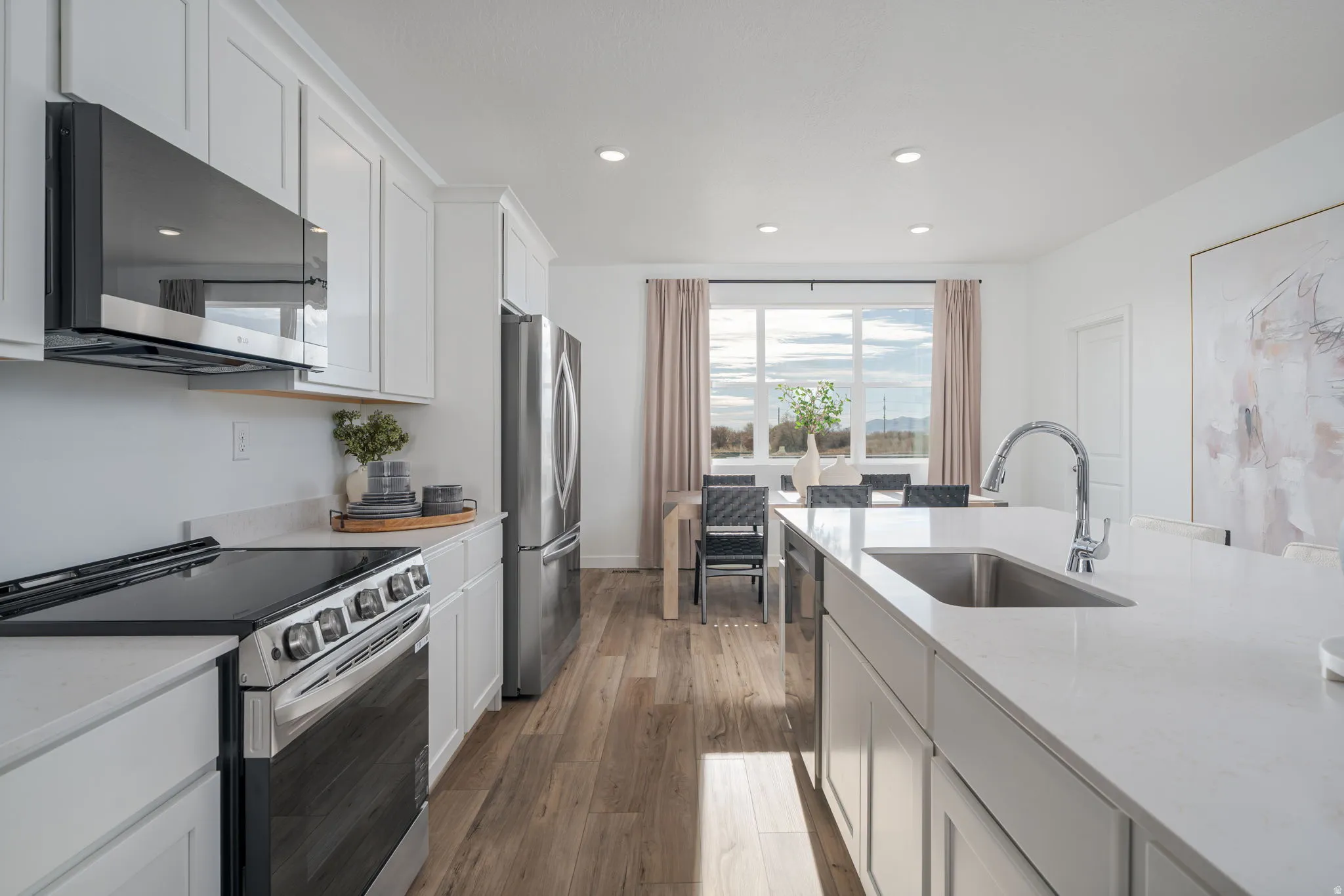 Modern kitchen featuring white shaker cabinetry, stainless steel appliances, light-toned countertops, and wood-finish flooring