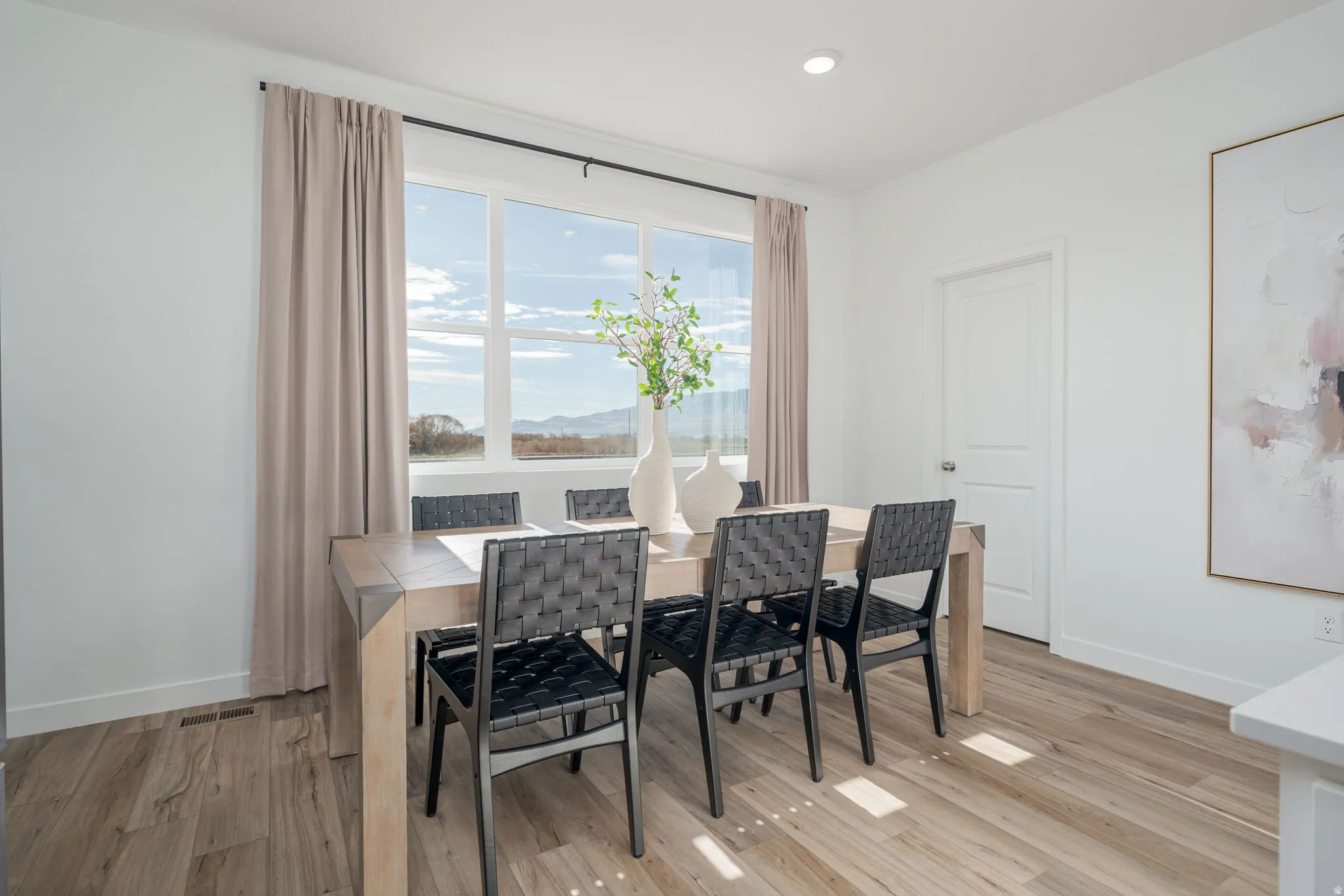 Dining area featuring a large picture window, recessed lighting, white trim, wood-finish flooring, and a white paneled door