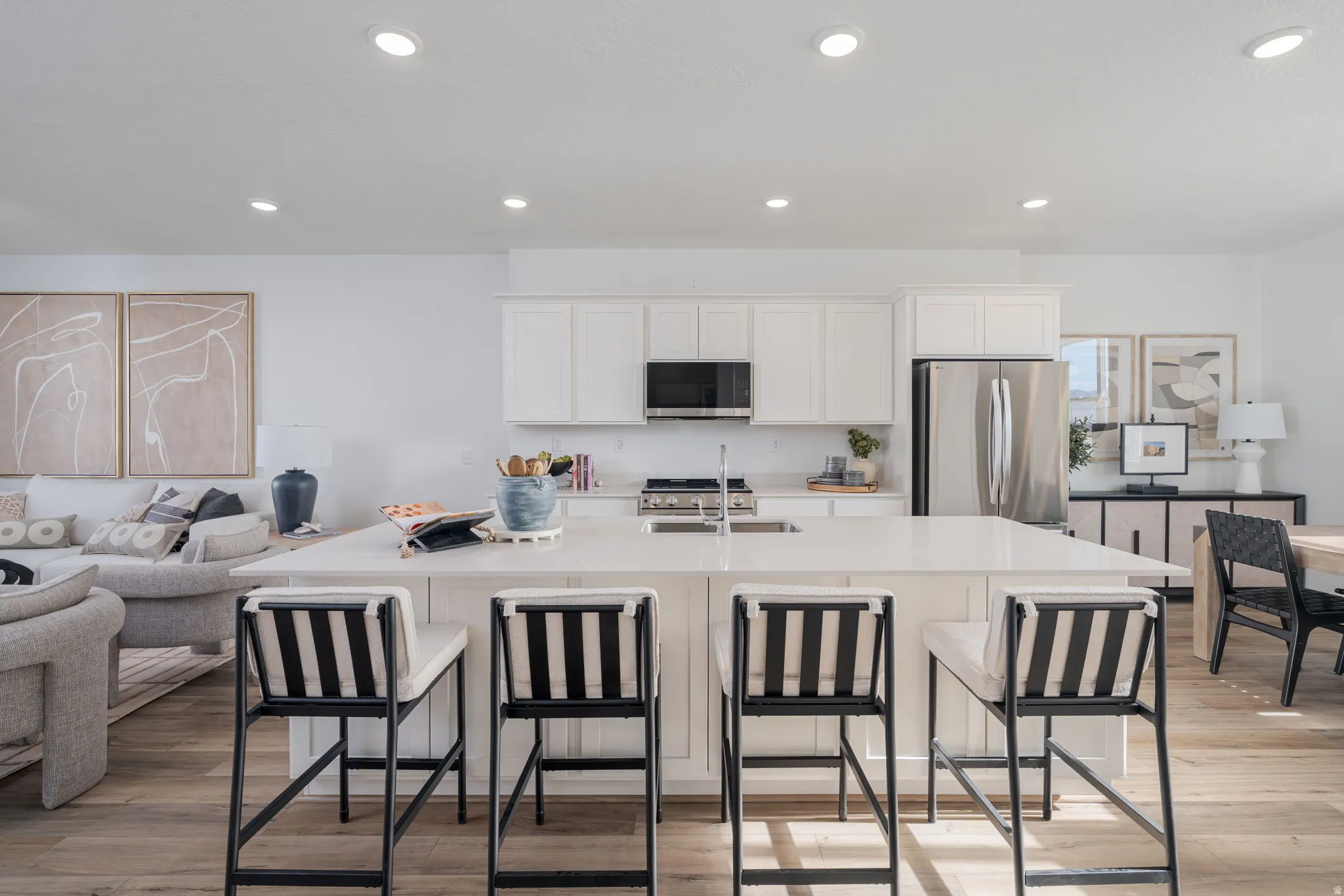 Open-concept kitchen featuring an oversized island with seating, white shaker cabinetry, stainless steel appliances, and wood-finish flooring