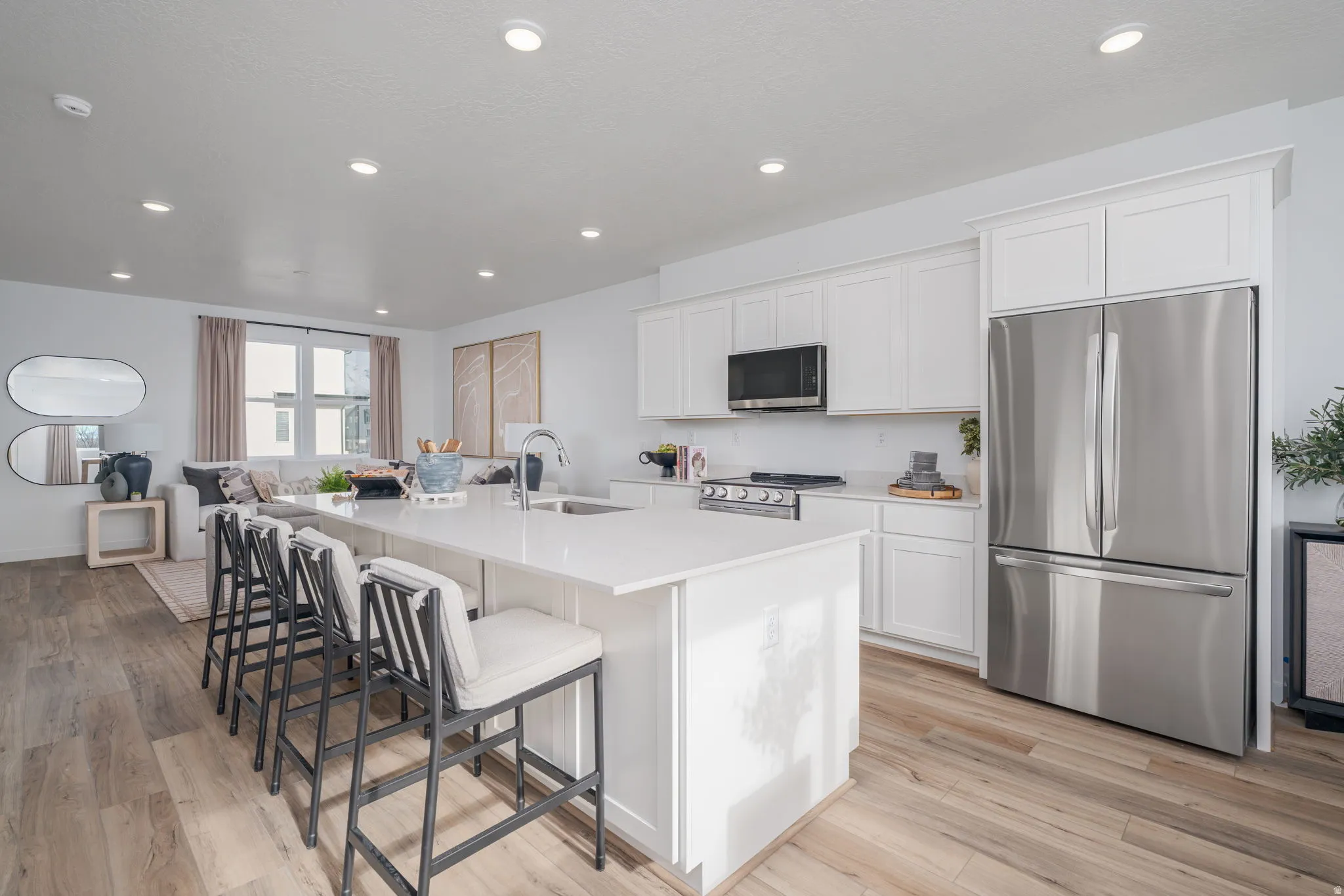 Open-concept living space featuring a kitchen with a large island, white cabinetry, stainless steel appliances, and wood-finish flooring
