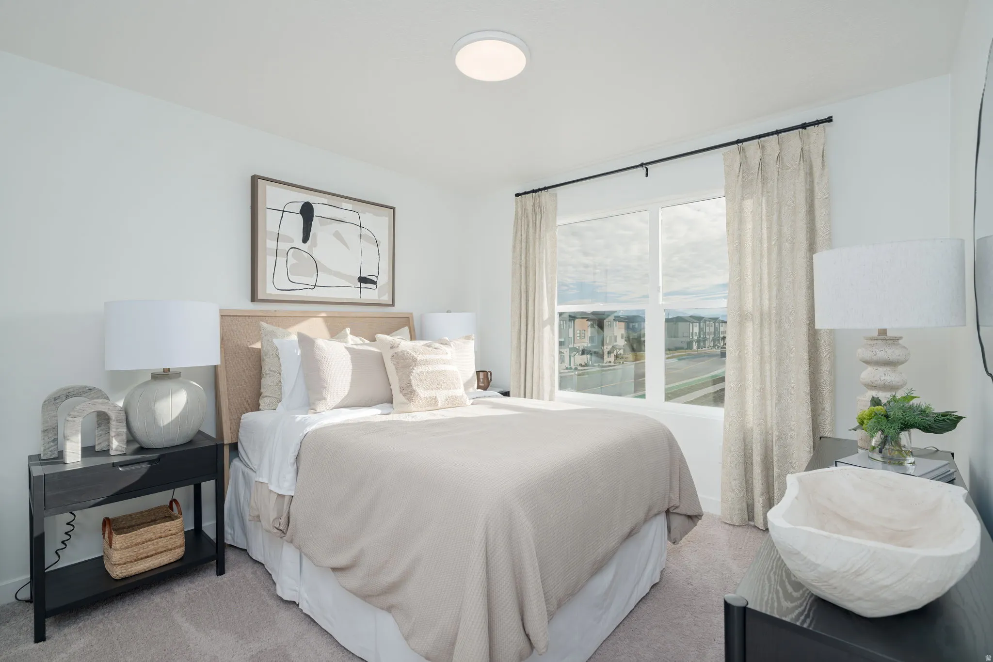 Bright bedroom featuring a large window, neutral carpeting, and a flush-mount ceiling light fixture