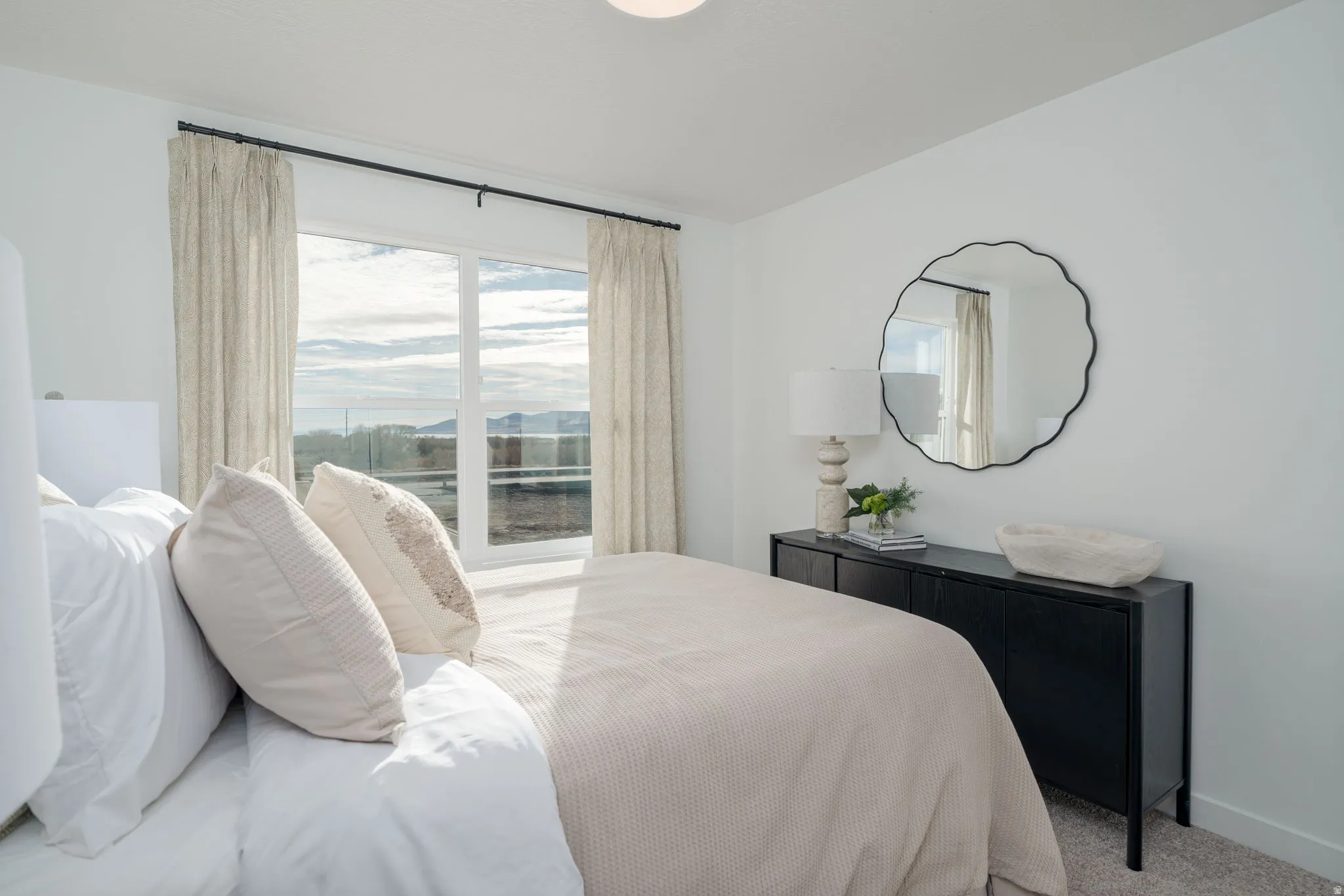 Bedroom featuring a large picture window, a deep black built-in console, and light-toned carpeting