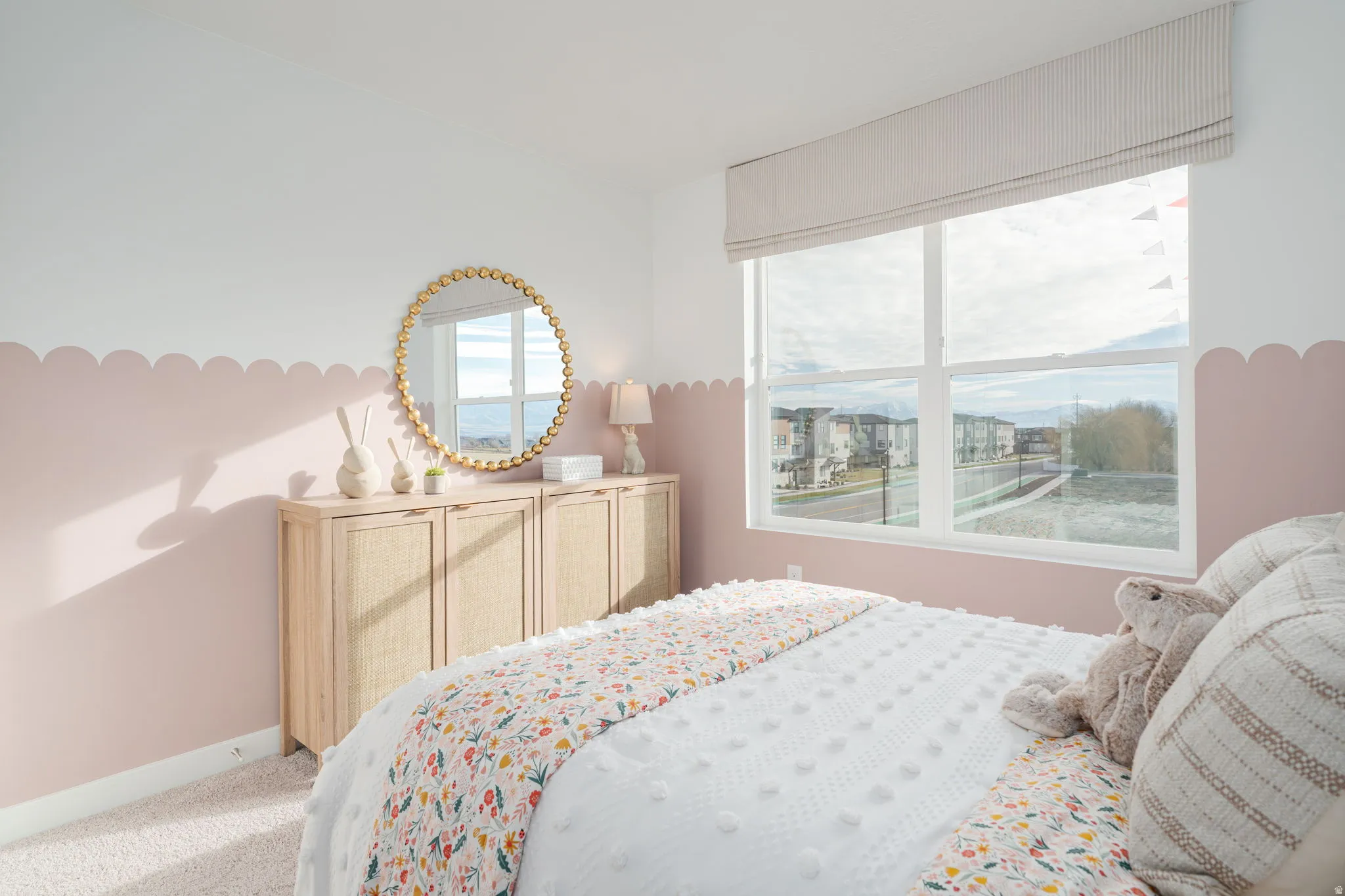 Room featuring a large window with a fabric Roman shade, light-tone carpeting, and two-tone wall treatment