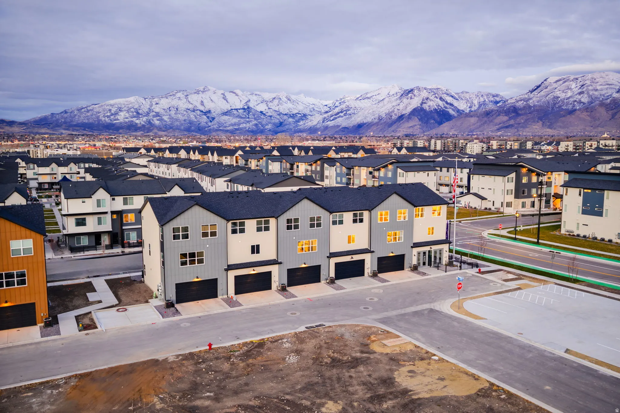 Modern townhome development with a mountain backdrop, featuring multi-story units, attached garages, and a paved street system