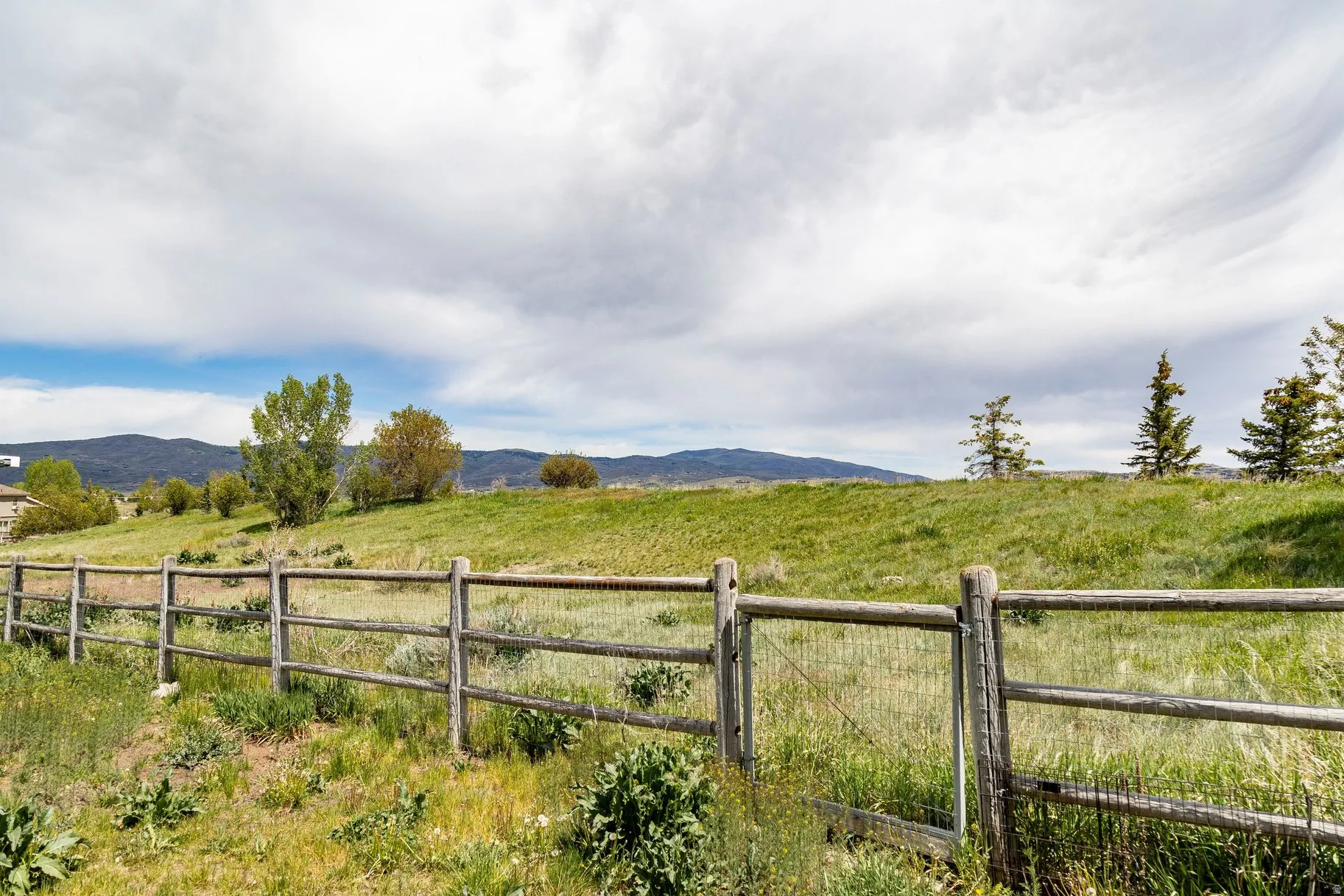 Expansive outdoor space featuring a rustic split rail fence and a verdant grassy slope