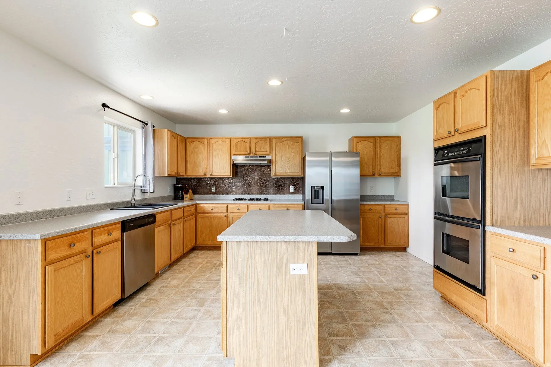 Kitchen featuring light wood cabinetry, a central island, stainless steel appliances, and recessed lighting