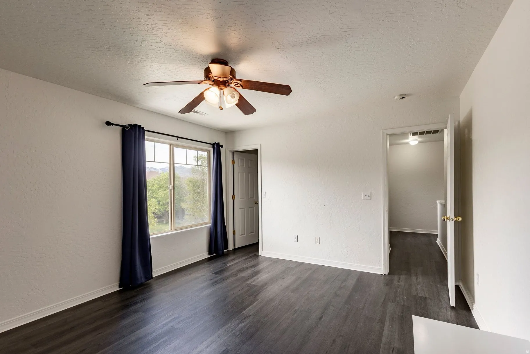 Spacious interior room featuring dark wood-finish flooring, white painted walls, and a ceiling fan with integrated lighting