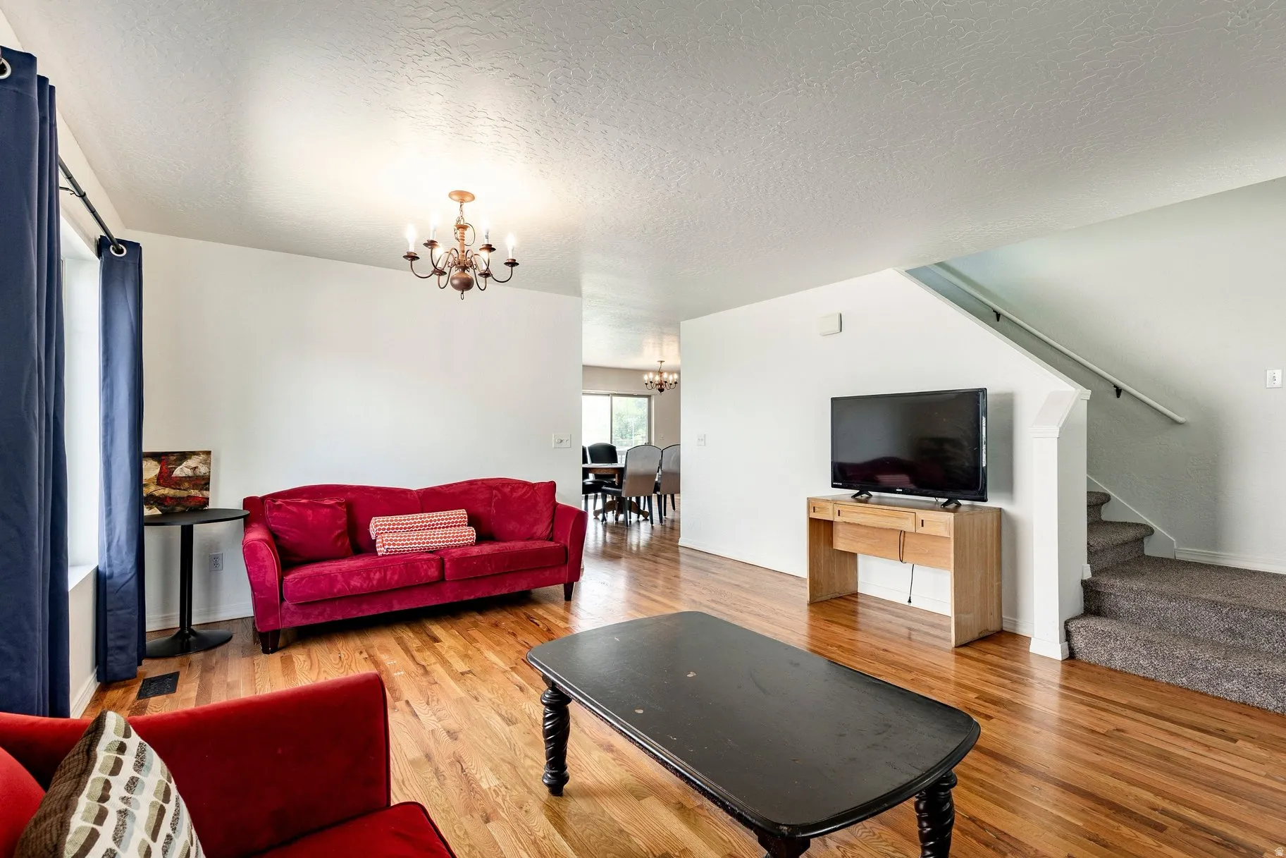 Bright living area featuring wood-finish flooring, a contemporary chandelier, and a carpeted staircase