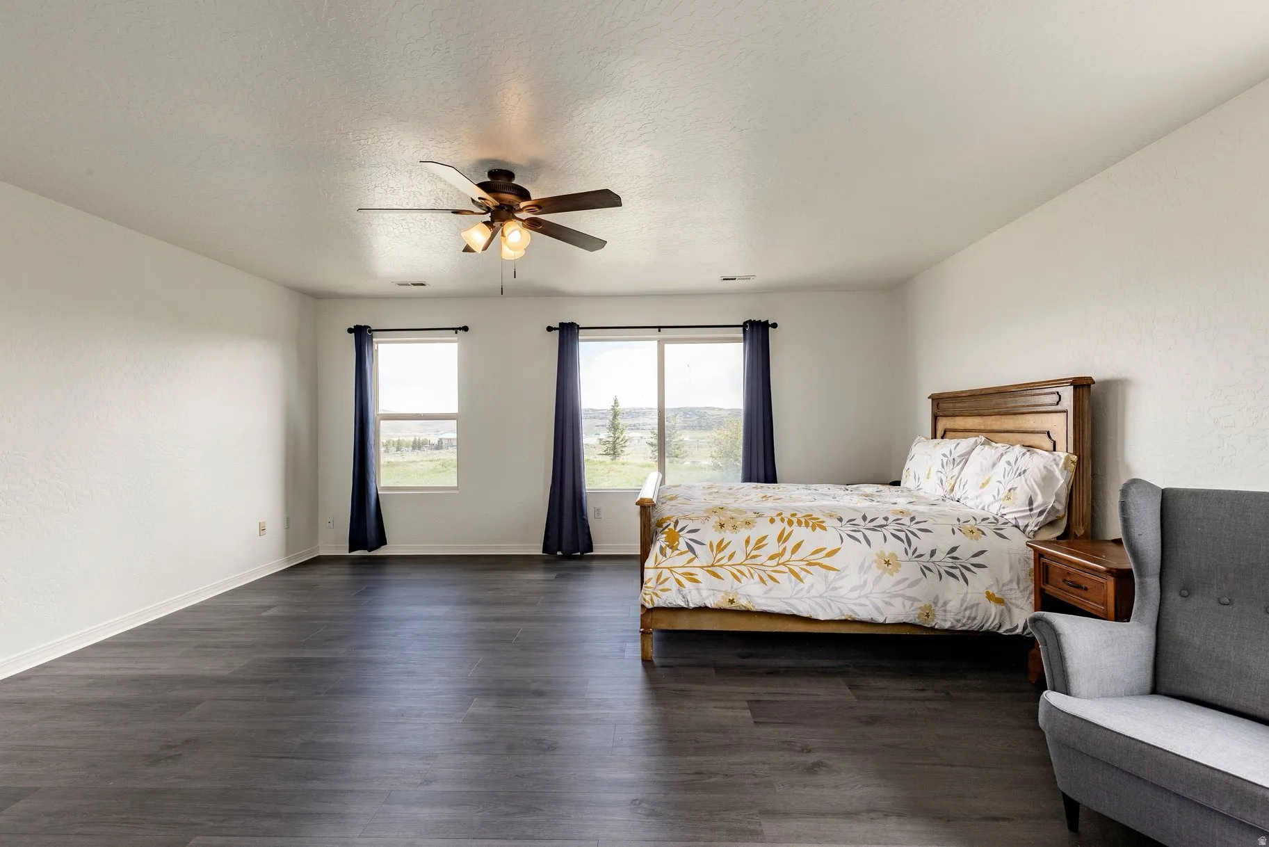 Spacious room featuring dark wood-finish flooring, white walls, and a ceiling fan with integrated lighting