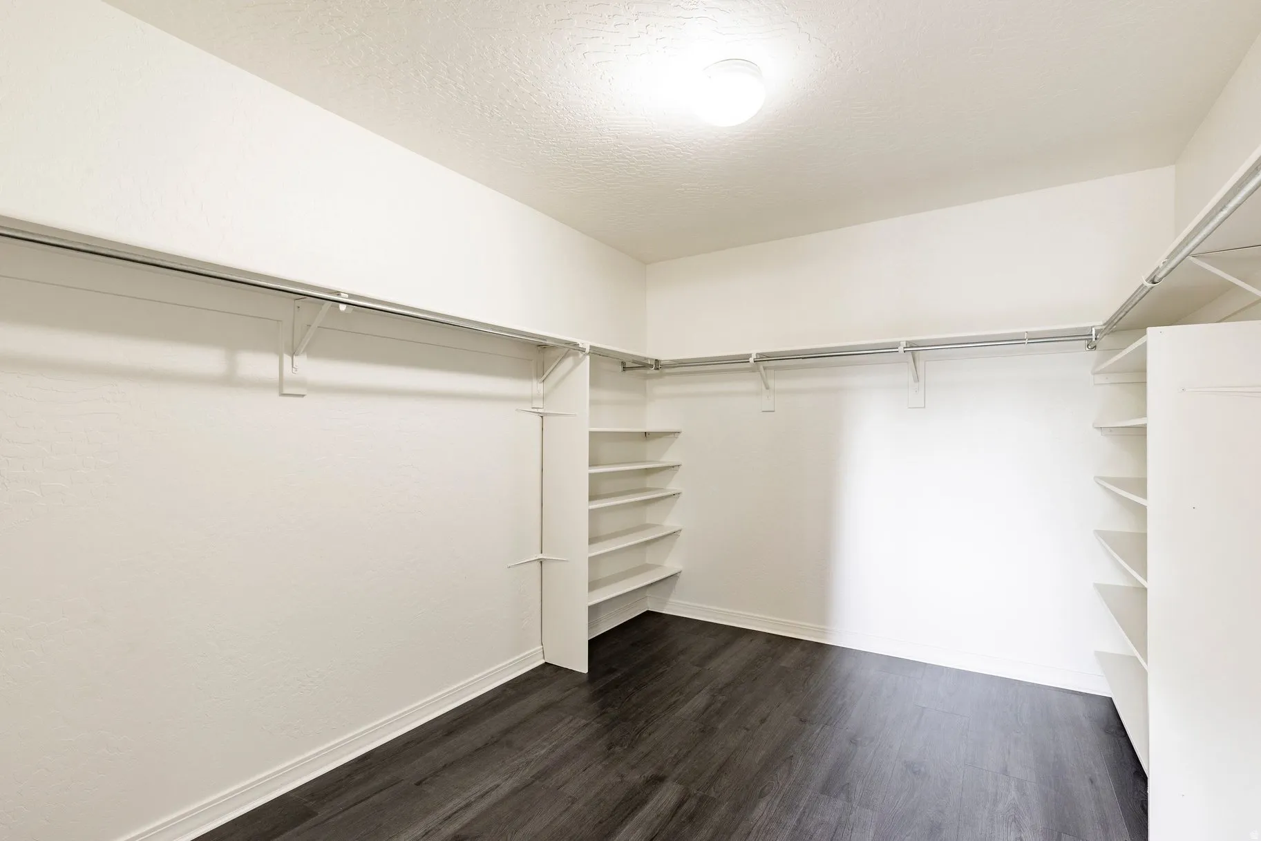 Spacious closet featuring dark wood-finish flooring, white walls, built-in shelving, and multiple clothing rods