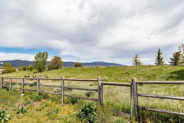 Expansive outdoor space featuring a rustic split rail fence and a verdant grassy slope