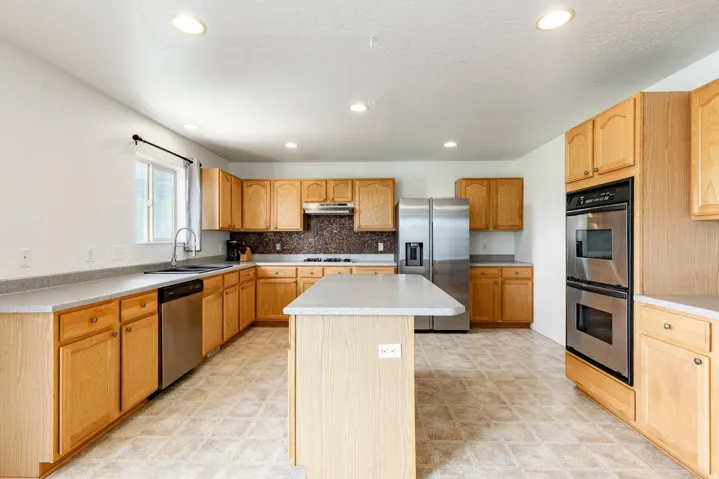 Kitchen featuring light wood cabinetry, a central island, stainless steel appliances, and recessed lighting