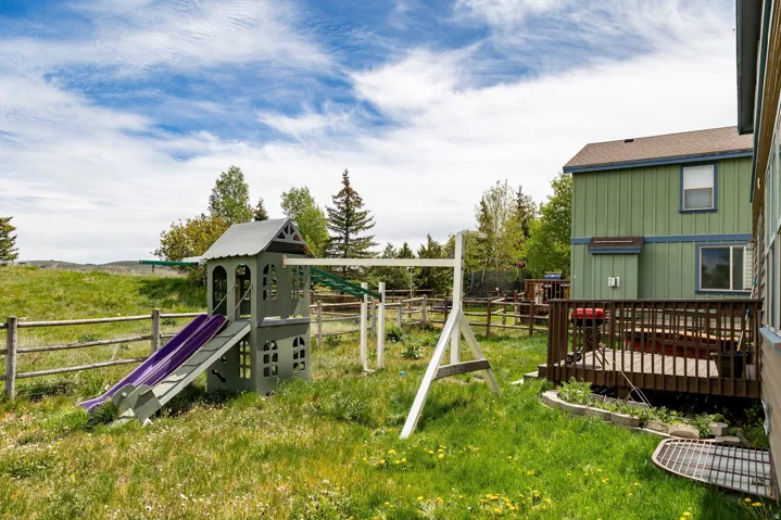 Expansive green space featuring a wooden split-rail fence, a raised wooden deck, and a two-story residential structure with green siding