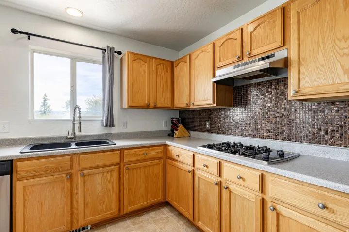 Kitchen featuring light wood cabinetry with silver hardware, light-toned countertops, and a modern mosaic tile backsplash
