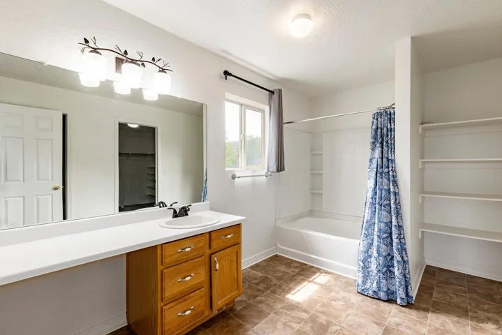 Bathroom featuring a vanity with a white countertop and wood-finish cabinetry, a large mirror, and a combined tub and shower unit