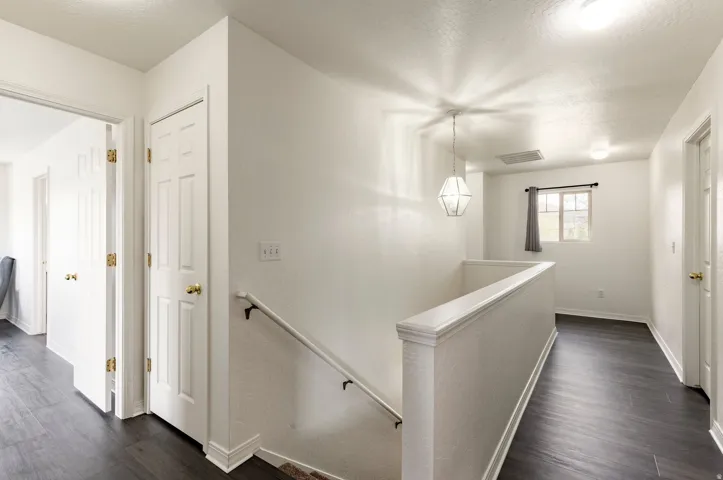 Second-level landing featuring wood-finish flooring, white walls, and a contemporary geometric pendant light fixture