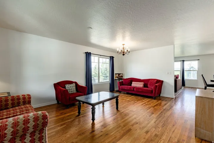 Hardwood flooring throughout a bright living area, featuring multiple large windows and a decorative chandelier