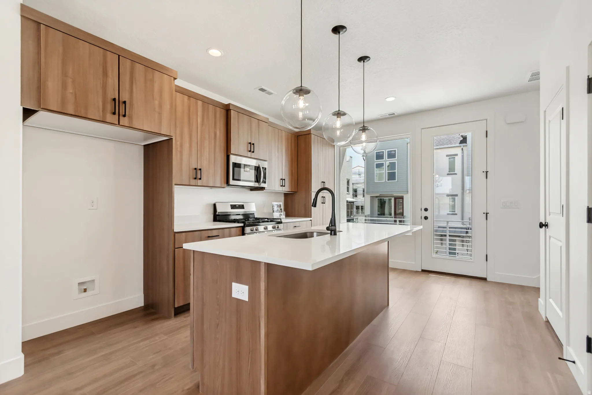 Modern kitchen featuring wood-grain cabinetry, stainless steel appliances, a center island with a sink and matte black faucet, and three pendant lights