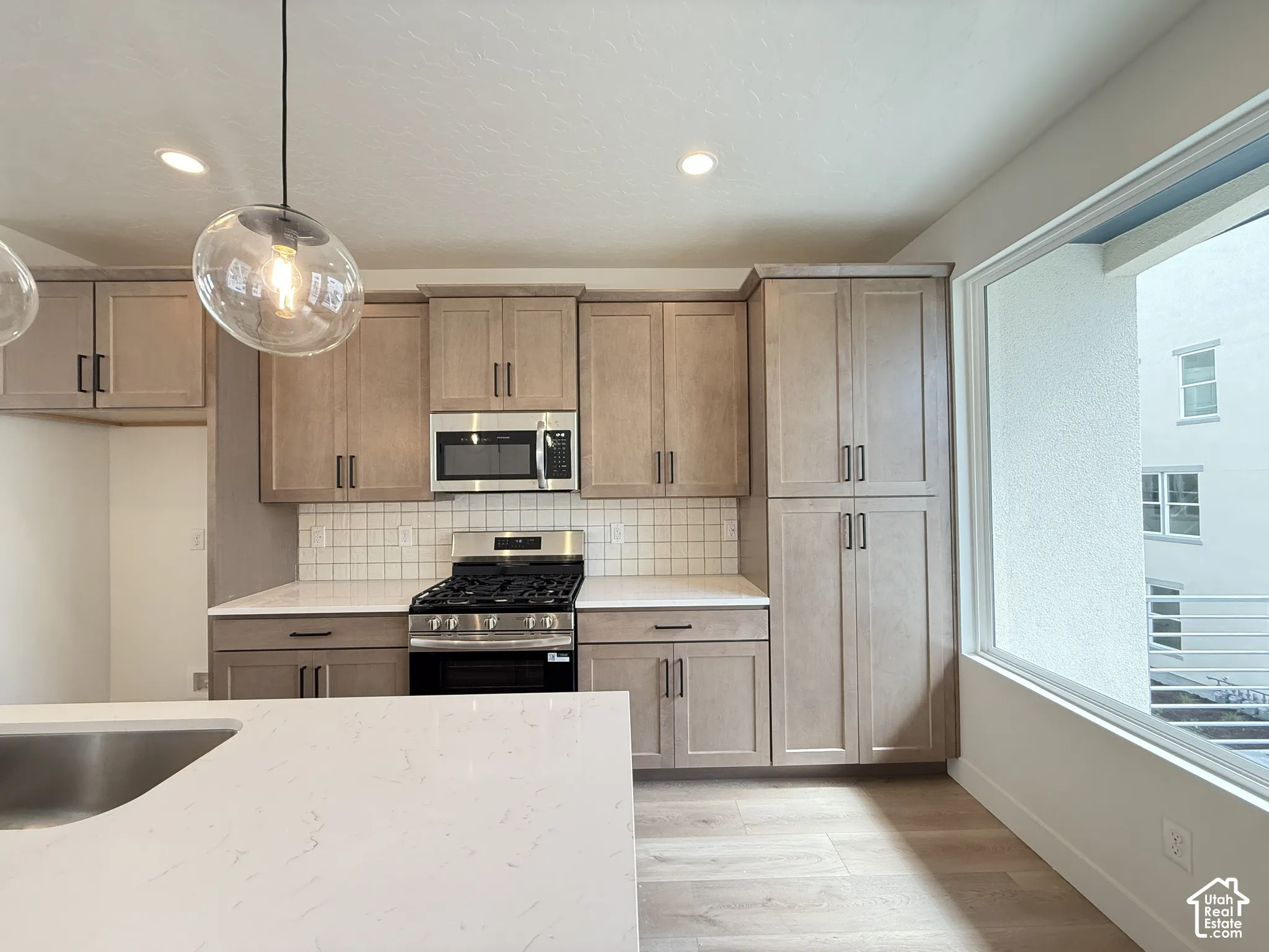 Kitchen featuring light wood-finish cabinetry, stainless steel appliances, a tile backsplash, and light countertops