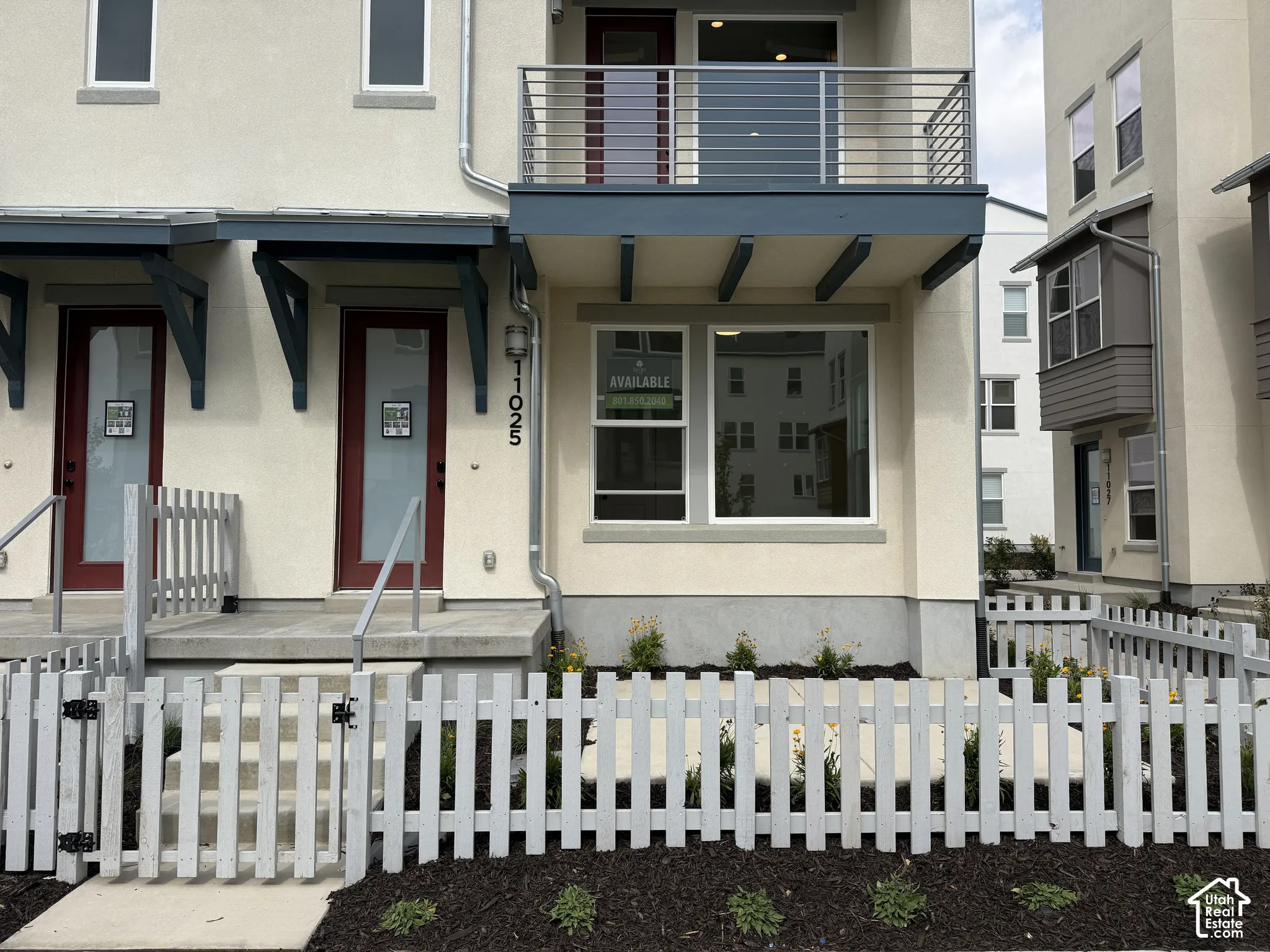Contemporary exterior with a balcony featuring metal railings and a white picket fence