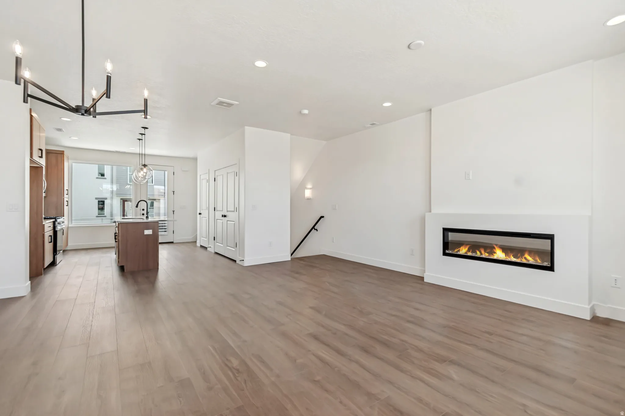 Open-concept living area featuring a linear electric fireplace, wood-finish flooring, recessed lighting, and a modern kitchen island with pendant lighting