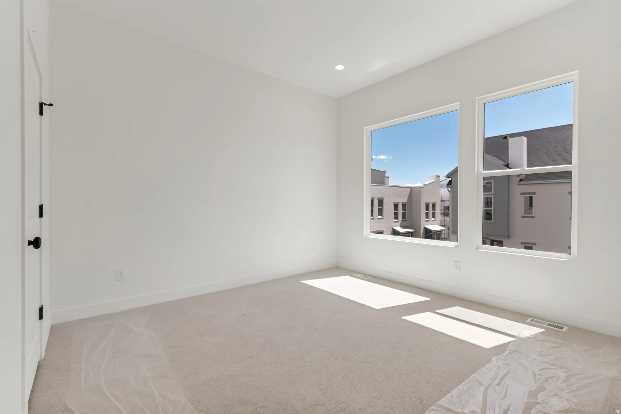 Bright room featuring dual windows with white trim, recessed lighting, neutral carpeting, and a white door with matte black hardware