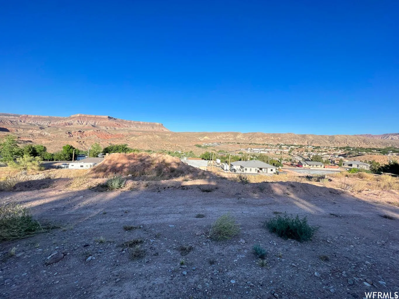 Expansive desert landscape with distant mountains, a small town nestled in the valley, and a clear blue sky