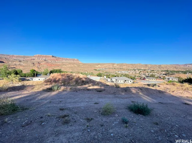Expansive desert landscape with distant mountains, a small town nestled in the valley, and a clear blue sky
